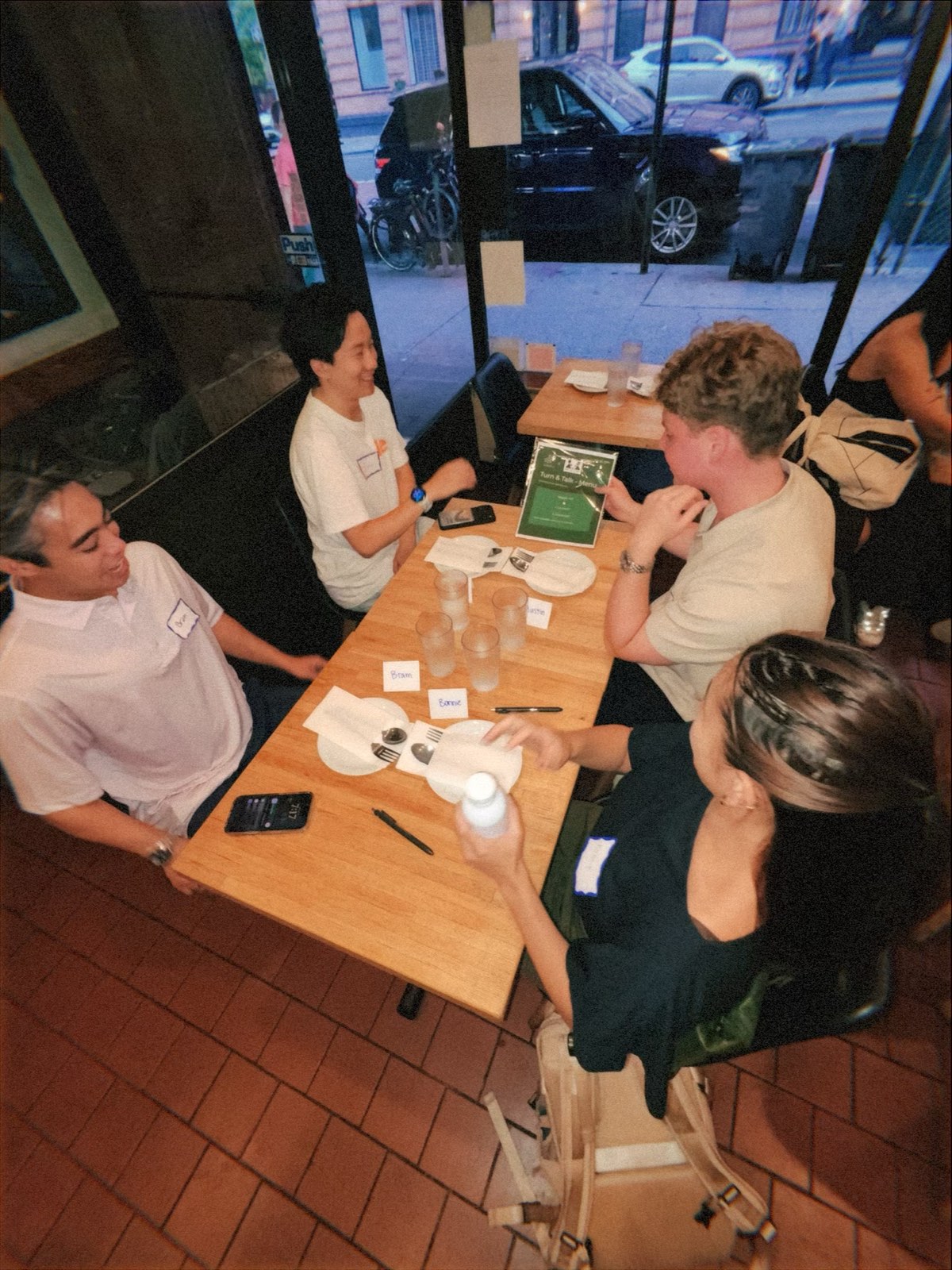 An overhead view of four attendees talking around a long table, with the event menu propped up and handwritten name cards in front of each seat.