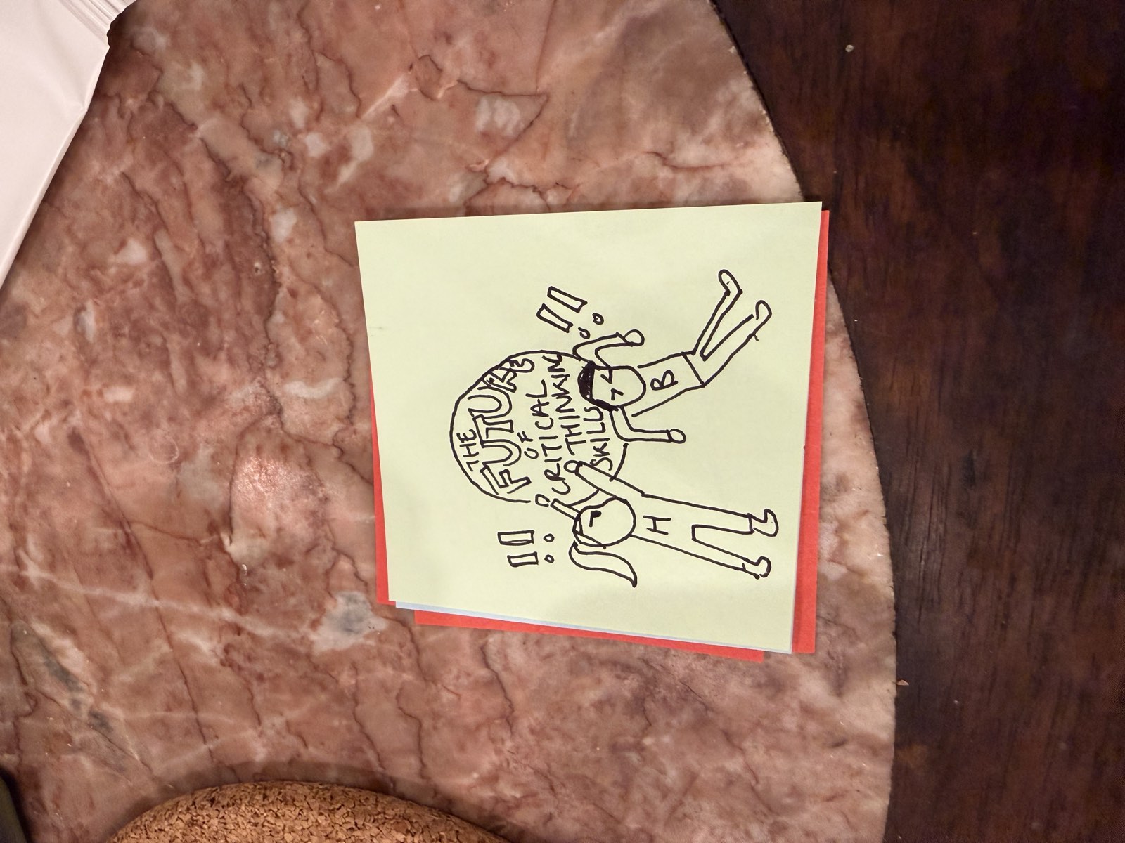 A hand-drawn sticky note left by an attendee: two stick figures holding up a large boulder labelled &ldquo;the future of critical thinking skills.&rdquo;